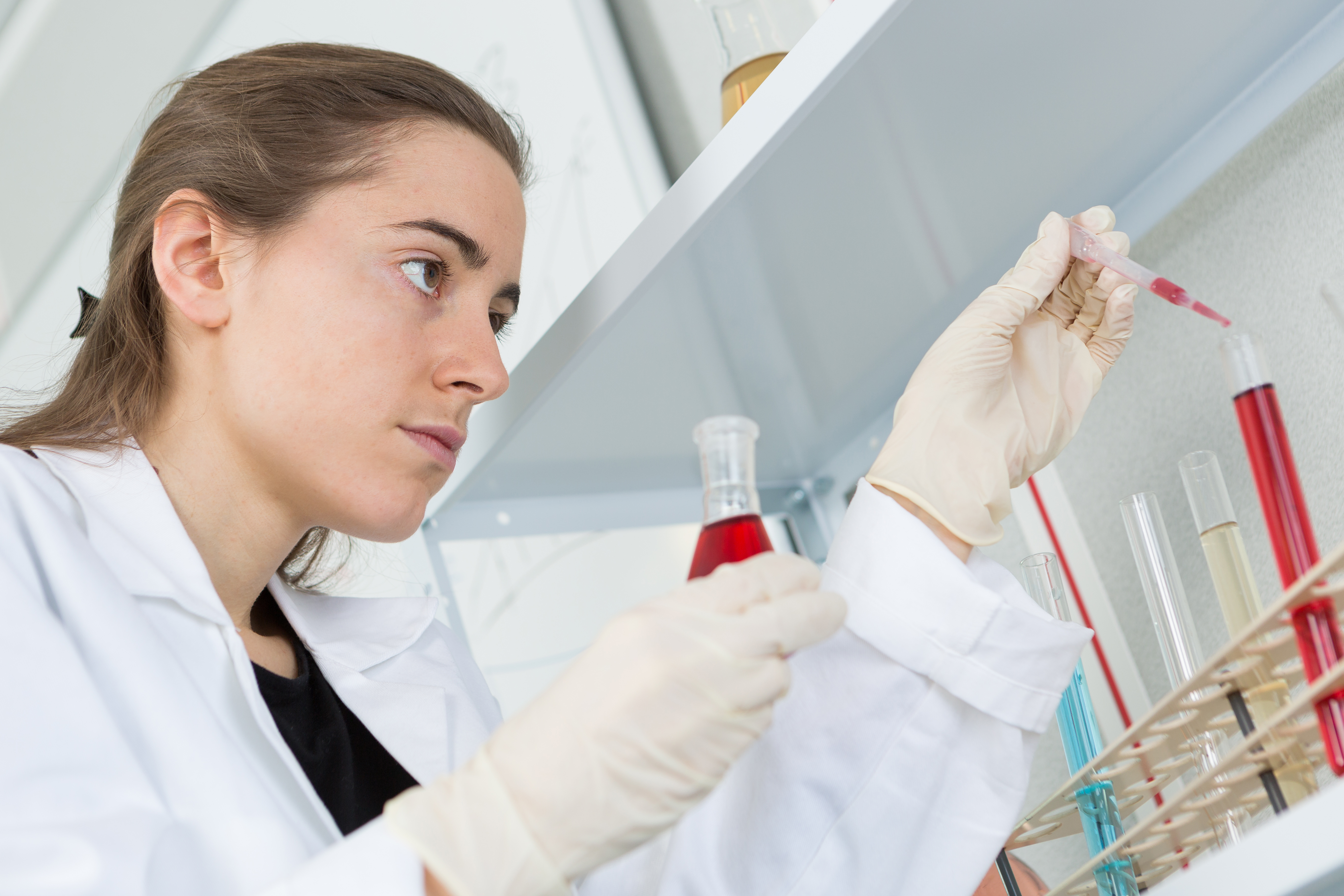 Kvindelig videnskabsmand drypper farvet væske fra pipette ned i reagensglas.