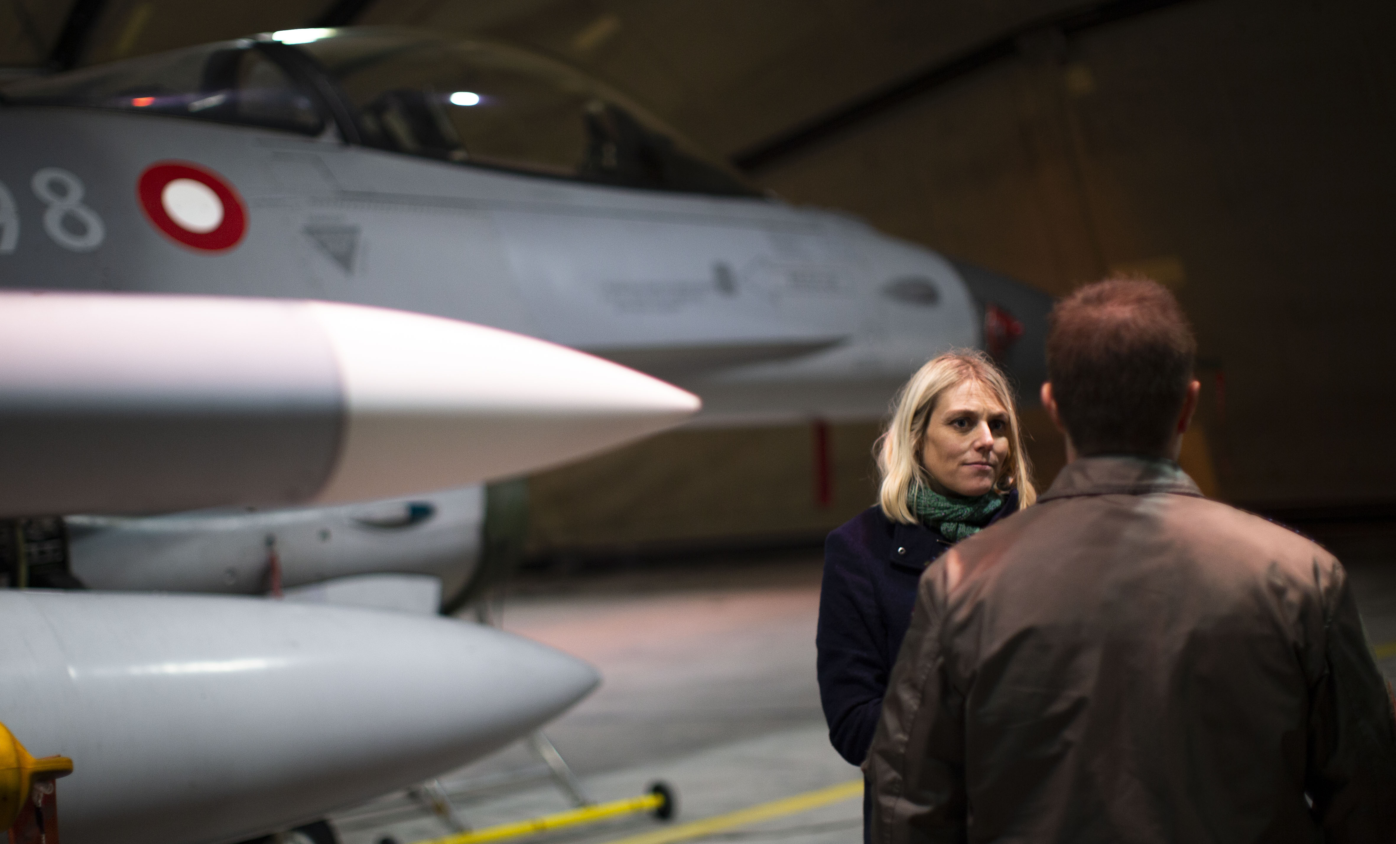 Forsvarsminister Trine Bramsen på militærbase i Litauen. Foran hende står en mand. Bag hende holder et jægerfly